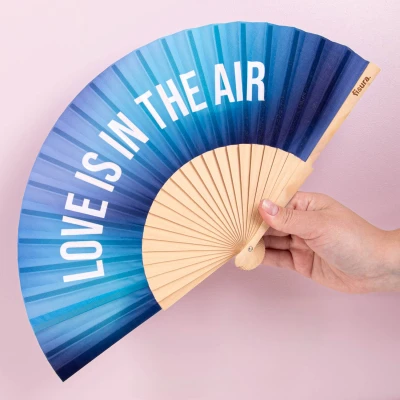 Afbeelding van Fisura Waaier met de tekst “love is in the air. Perfecte bruiloftsventilator van hout een blauw kleurverloop. Inclusief hanger. Afmetingen: 42,5 x 23 cm.
