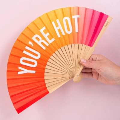 Afbeelding van Fisura Waaier met de tekst “you are h*t. Originele houten handventilator een roze oranje kleurverloop. Ophangkoord inbegrepen. Afmetingen: 42,5 x 23 cm.