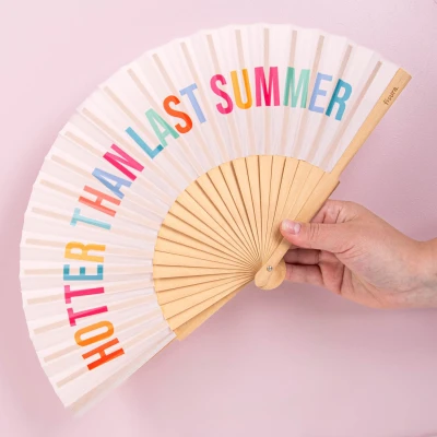 Afbeelding van Fisura Waaier met de tekst “hotter than last summer. Beige handventilator speelse veelkleurige letters. Ophangkoord inbegrepen. Afmetingen: 42,5 x 23 cm.
